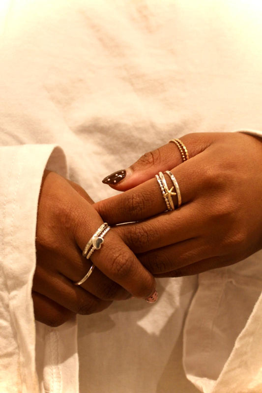 Close-up of hands with multiple rings on a light background all of the rings are stacking rings across the entire collection
