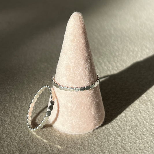 Two silver rings on a cone-shaped pink stand against a neutral background