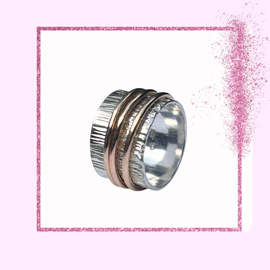 A sterling silver spinner ring with a textured band, displayed against a pink glittery background.