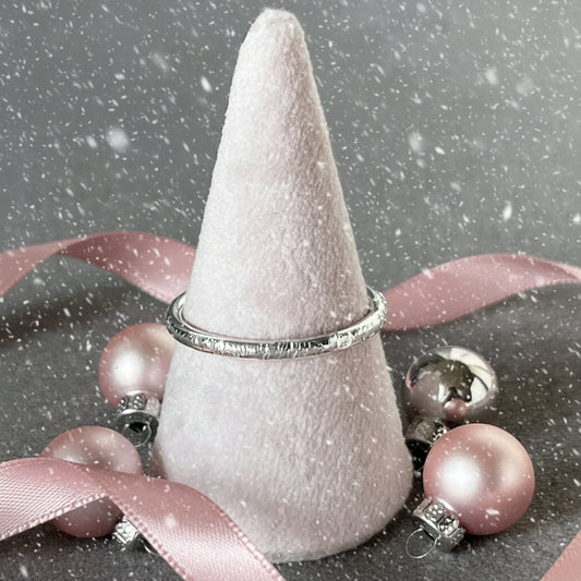 Silver ring on a white cone-shaped stand against a gray background