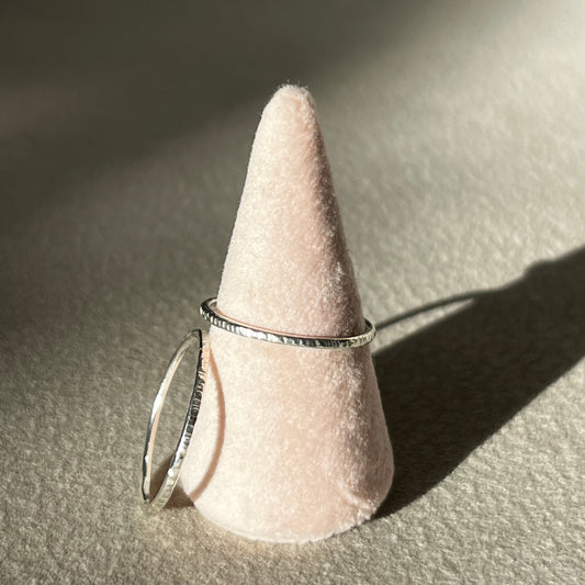 Silver ring on a cone-shaped pink stand against a neutral background