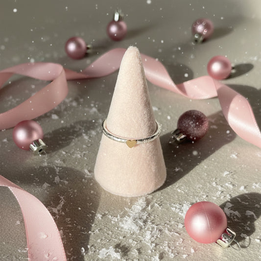 Ring on a pink cone-shaped stand with a heart detail on a beige background