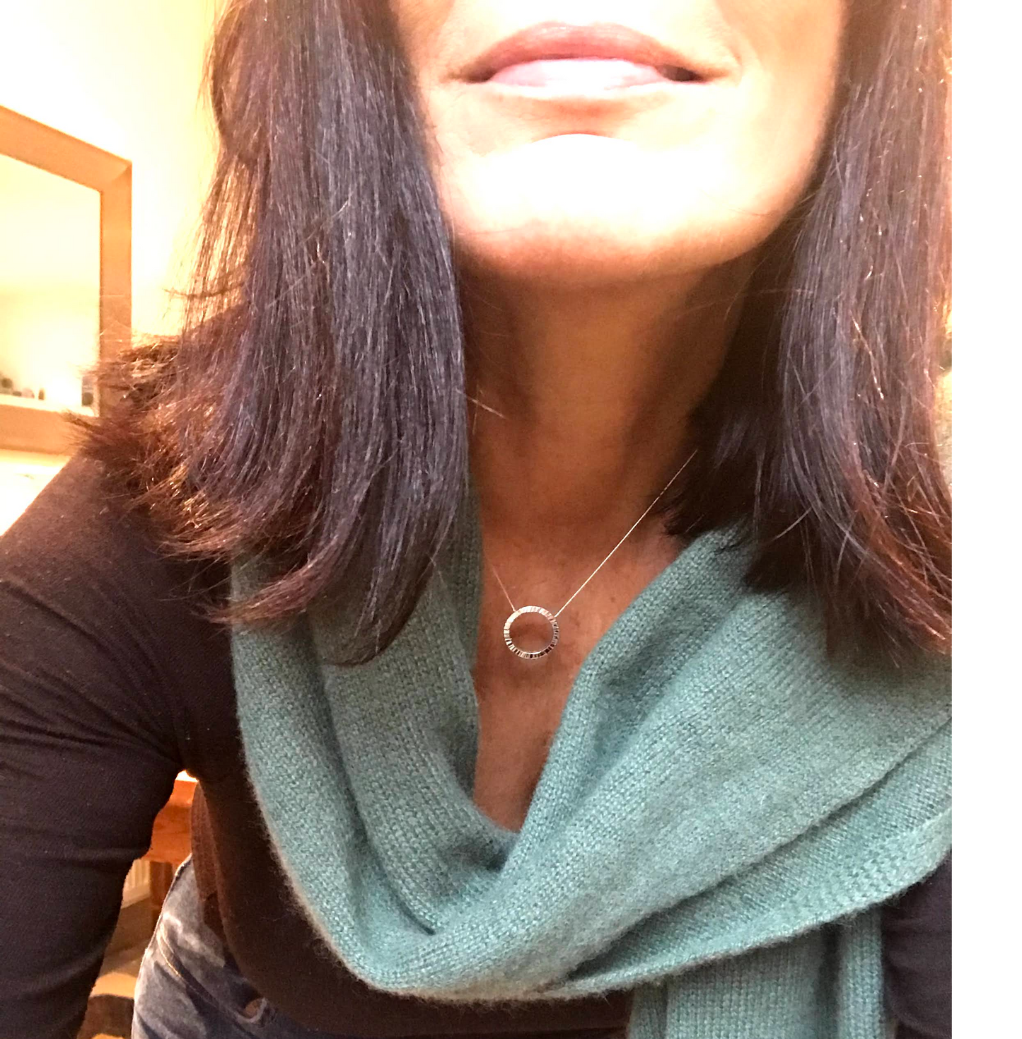 Handmade sterling silver 20cm circle of silver made from 2mm square wire suspended on a hidden bale behind the circle. The circle appears to float on a sterling silver diamond cut curb chain Model/silversmith pictured wearing the pendant and a green scarf made in Dublin Ireland