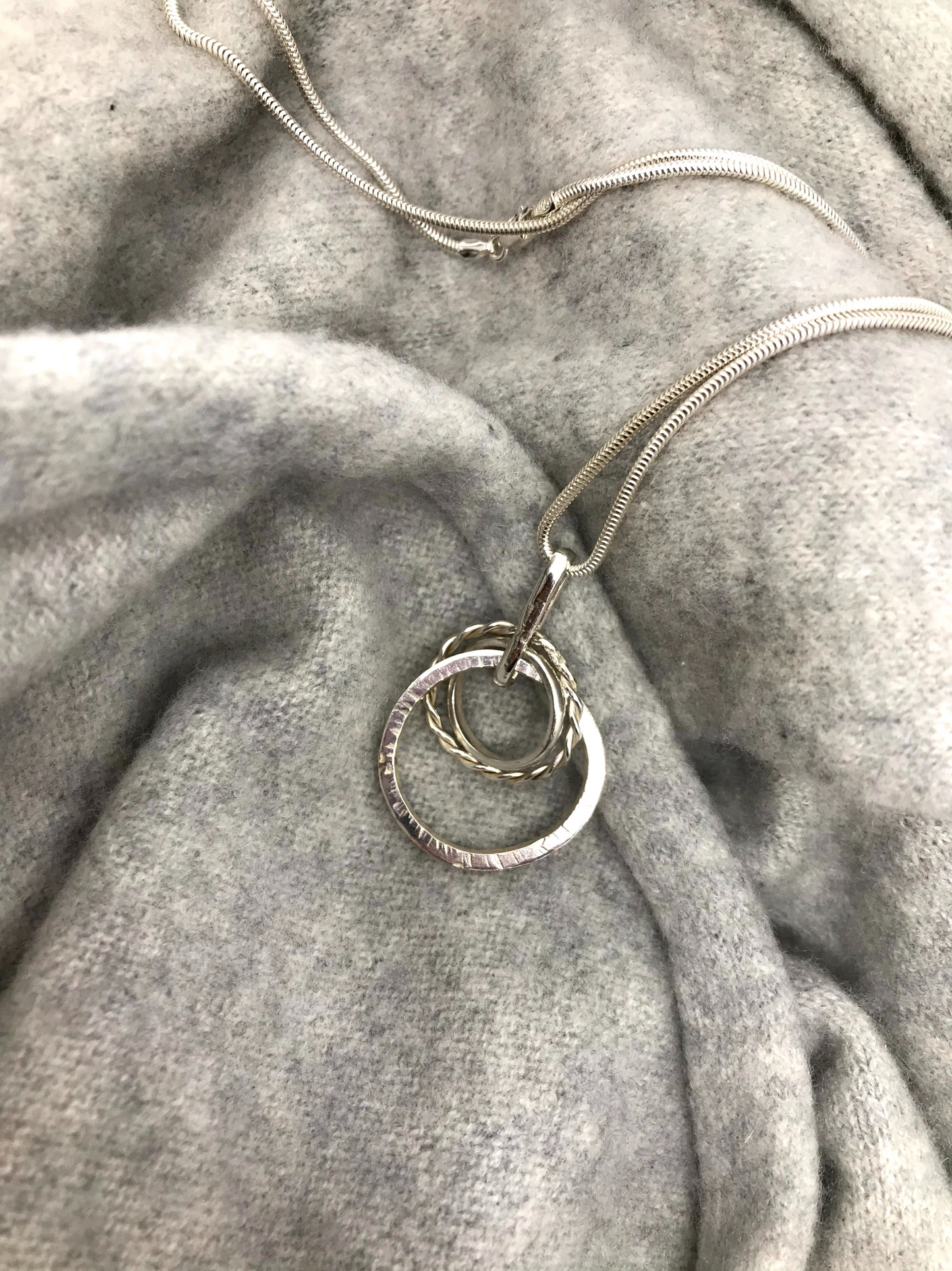 three circles intertwined twisted hammered and mirror 40cm snake chain sterling silverSterling silver mixed loop necklace. Three circles of silver. One hammered, one twisted and one polished. Hangs on a sterling silver snake chain with a secure 'lobster claw' closing clasp.