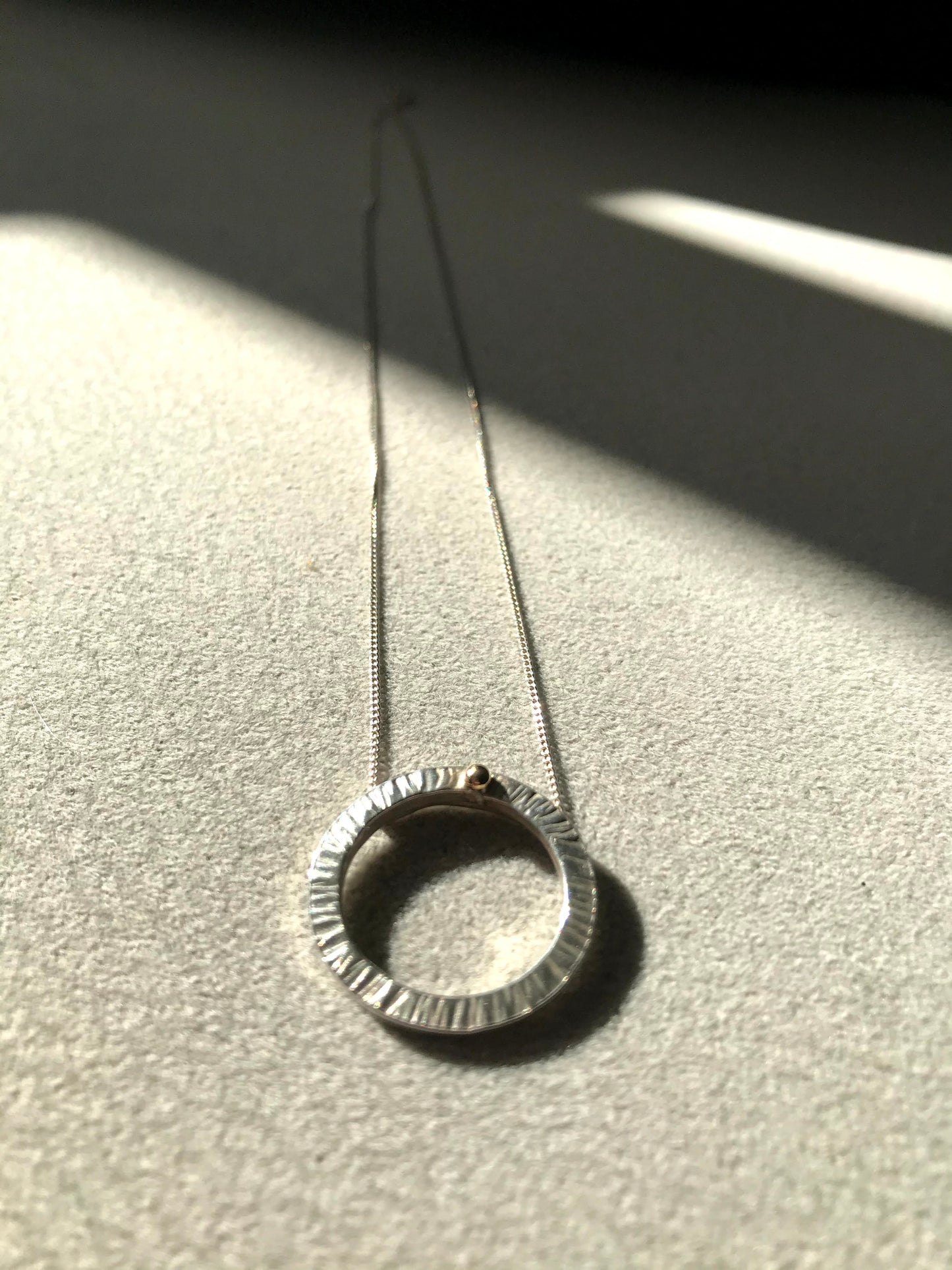 Handmade sterling silver 16mm diameter circle - hammered finish to represent rays of the sun hence the name 'Rise' - this little pendant is suspended on a sterling silver diamond cut curb chain 40cm or 45cm length. The piece is complete with a ball of 9ct gold so you can Rise with gold.