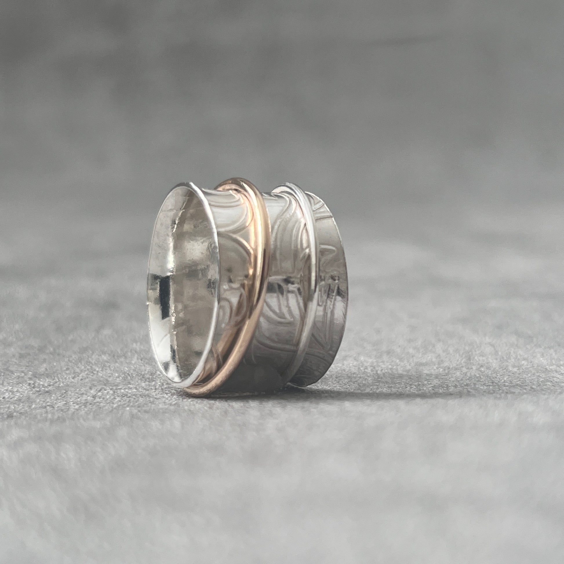 stg silver spinner ring one thick band 11mm wide with . Over it spins a silver beaded thin ring 1.5mm wide. Leafy imprinted pattern hand embellished surface on main ring, two spinner rings on the outer surface one silver one gold filledThe outer ring spins with your touch