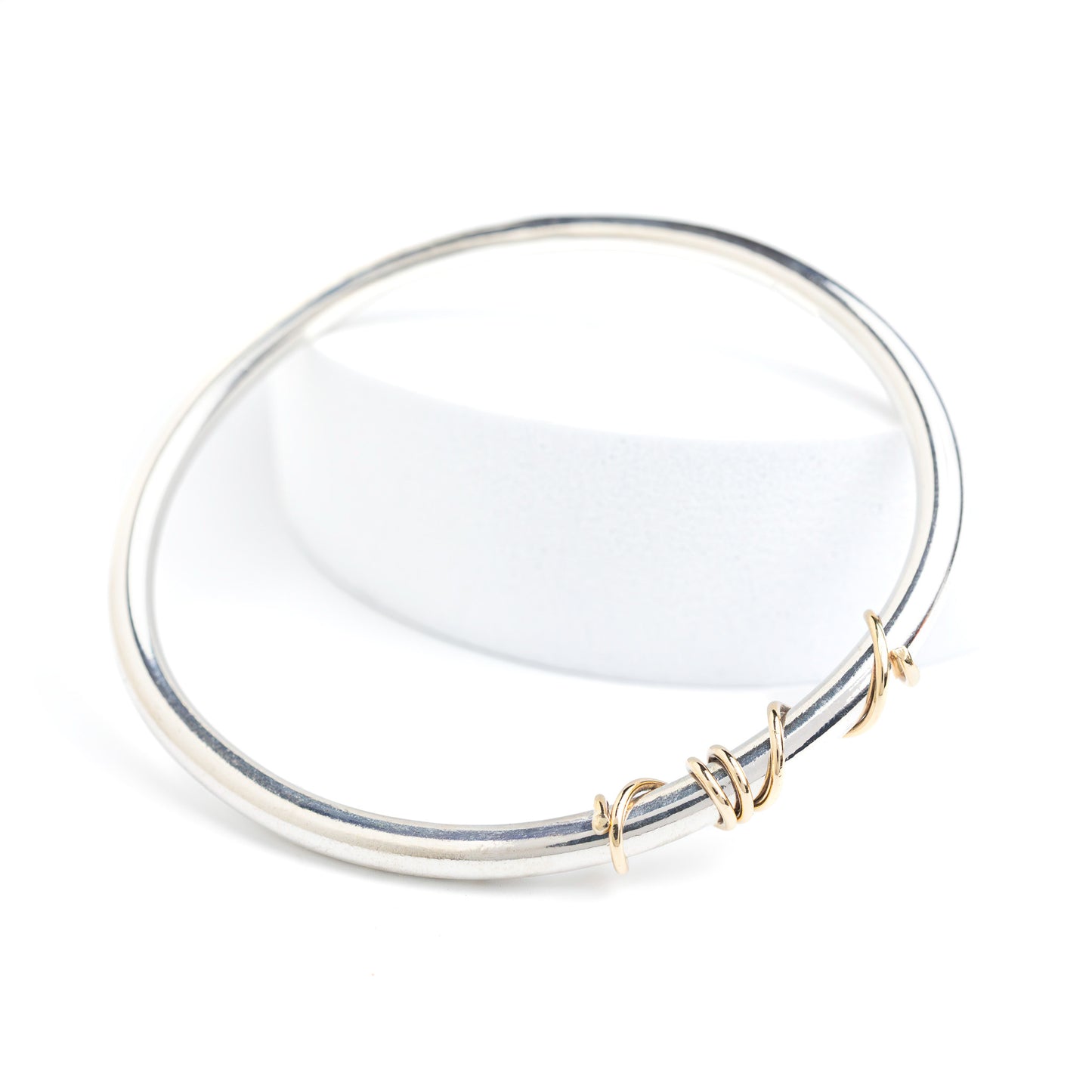 handmade sterling silver solid bangle with 9ct gold wrap of wire twisted around the front of the bangle on a white out background