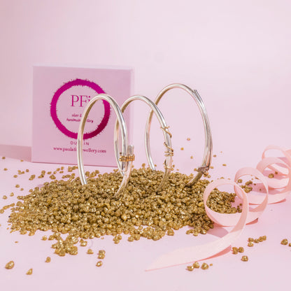 three sterling silver bangles with the presentation box which is pink and grains of gold decorations in the foreground