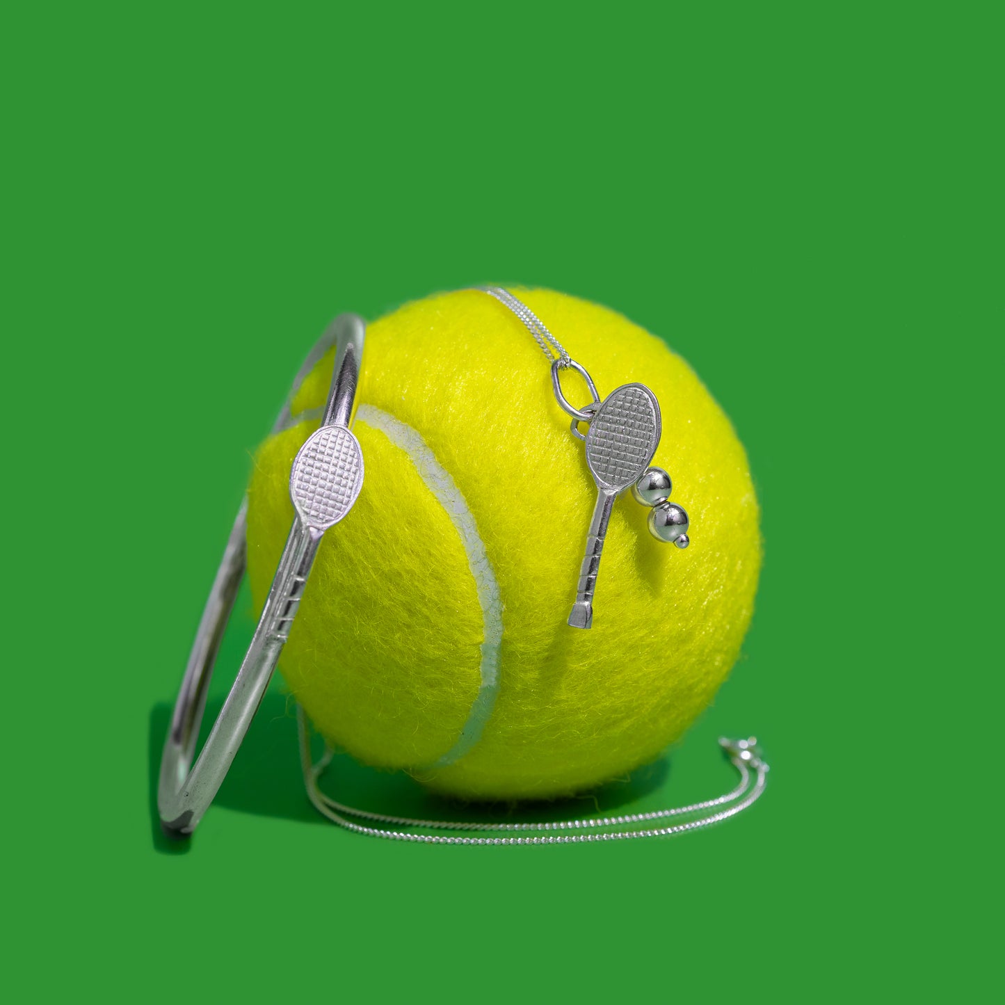 Sterling silver bangle and sterling silver tennis pendant on a green tennis ball with green background