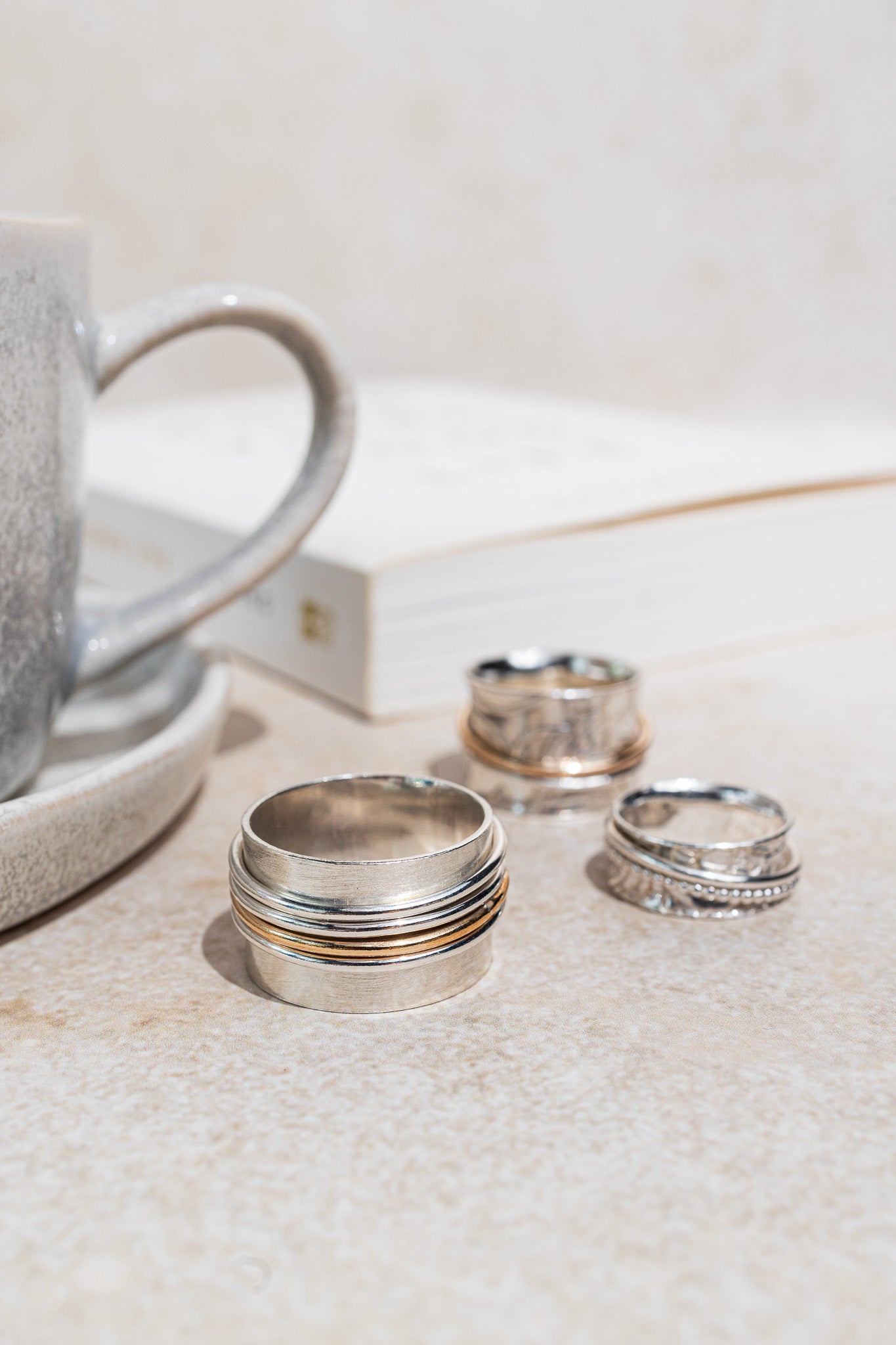 stg silver spinner ring one thick band 8mm wide with an imprinted paisley pattern. Over it spins a silver beaded thin ring 1.5mm wide. The outer ring spins with your touch pictured here with a book and a mug
