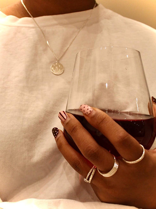 Hand holding a glass of red wine with a white shirt and necklace in the background