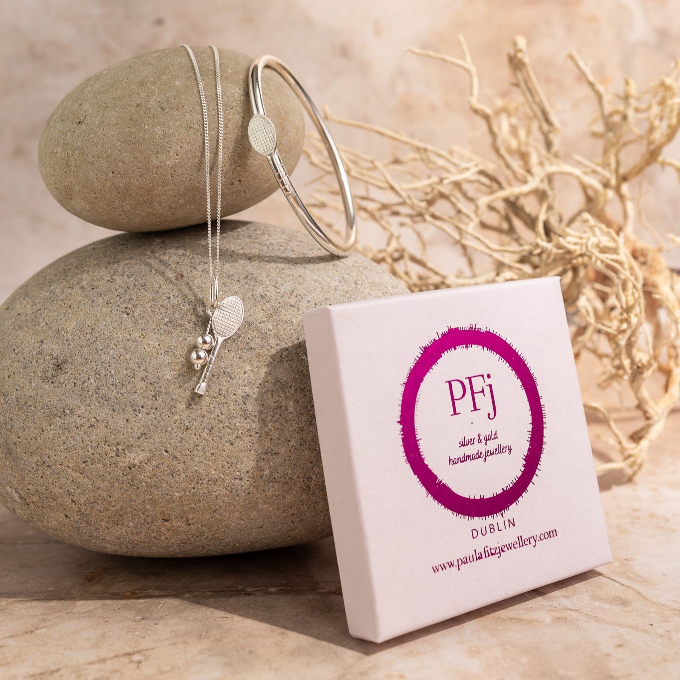 Display showing the gift box, pink with logo also tennis bangle and tennis pendant displayed on a brown sandstone rock