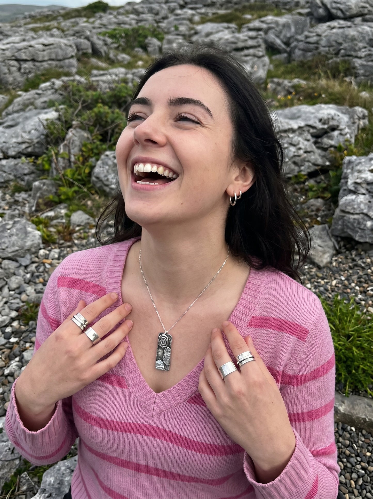Woman in a pink sweater laughing outdoors with rocky landscape