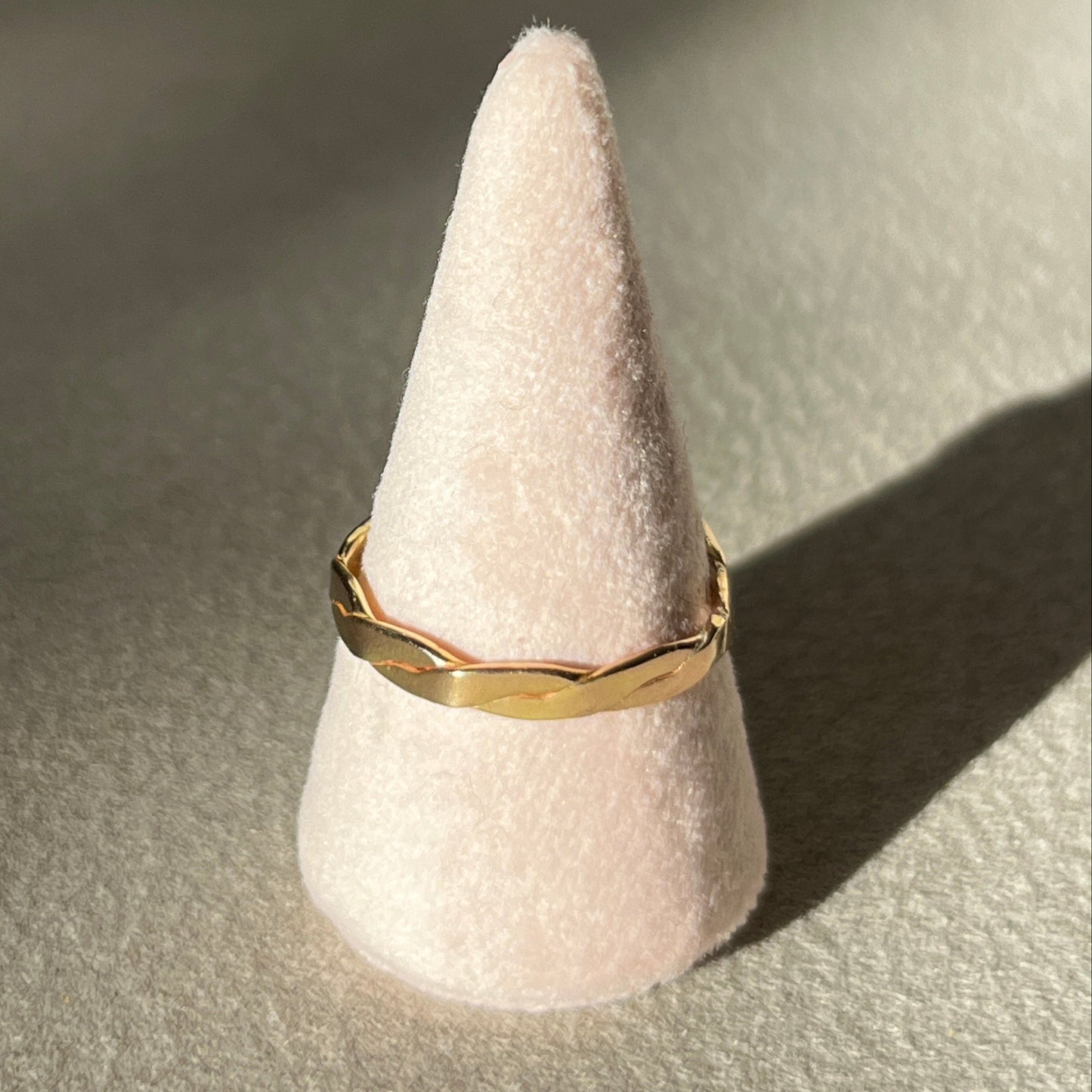 Gold ring on a cone-shaped white stand against a neutral background