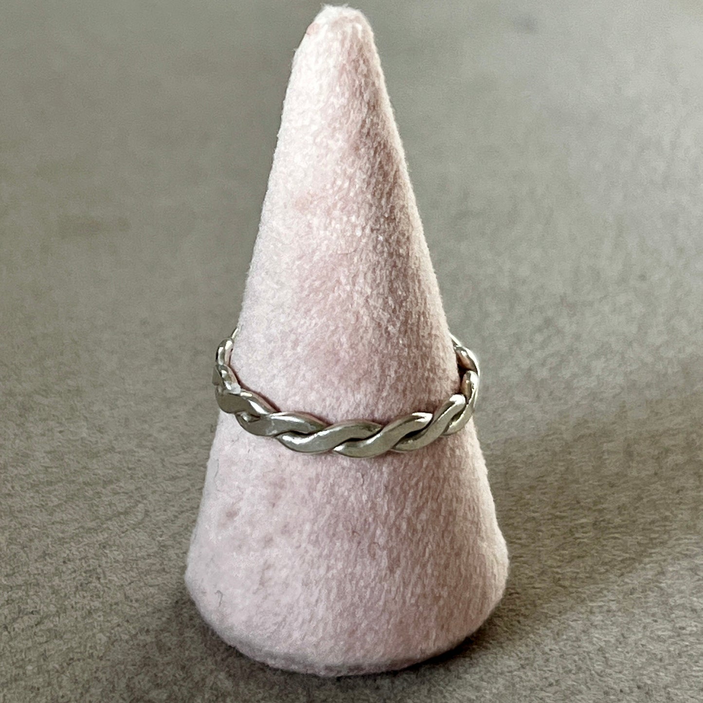 Silver braided ring on a cone-shaped pink stand against a gray background