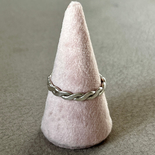 Silver braided ring on a cone-shaped pink stand against a gray background