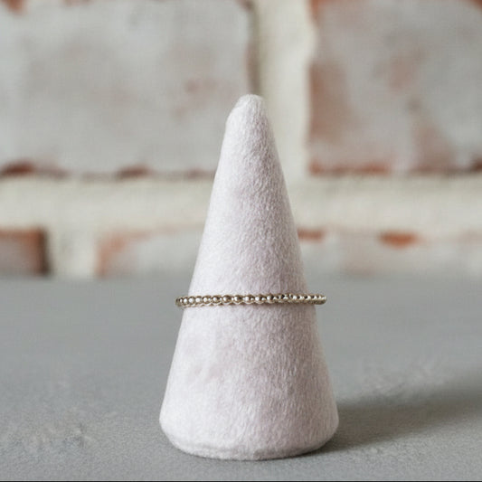 Gold ring on a textured cone-shaped stand against a gray background