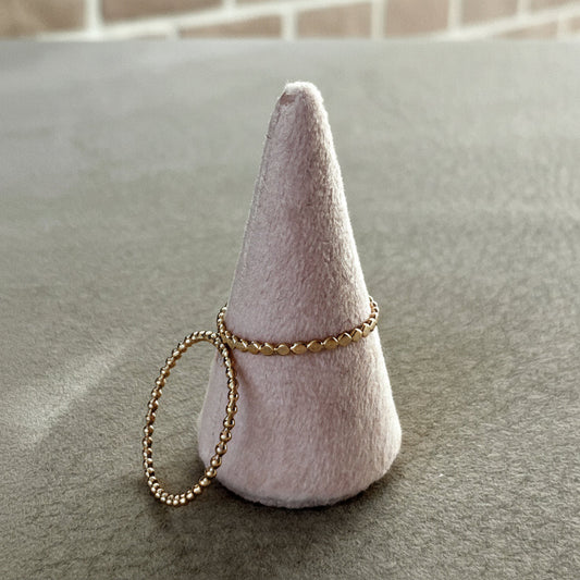 Two gold bracelets on a cone-shaped felt holder against a neutral background