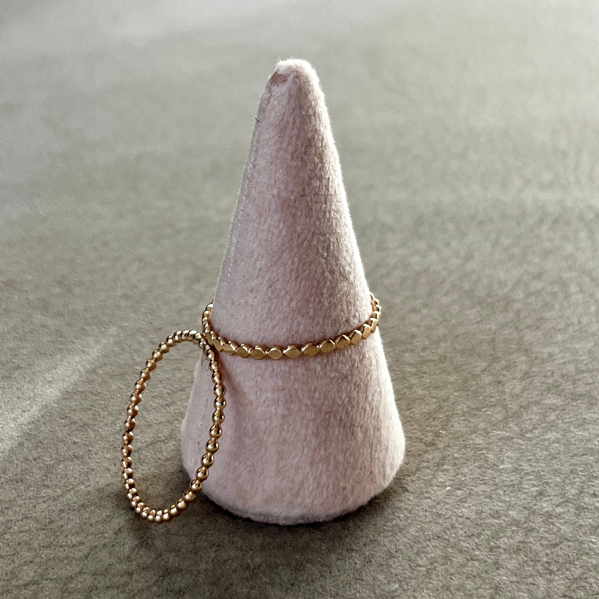 Two gold rings on a cone-shaped felt stand against a neutral background