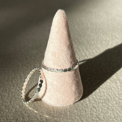 Two silver rings on a cone-shaped pink stand against a neutral background