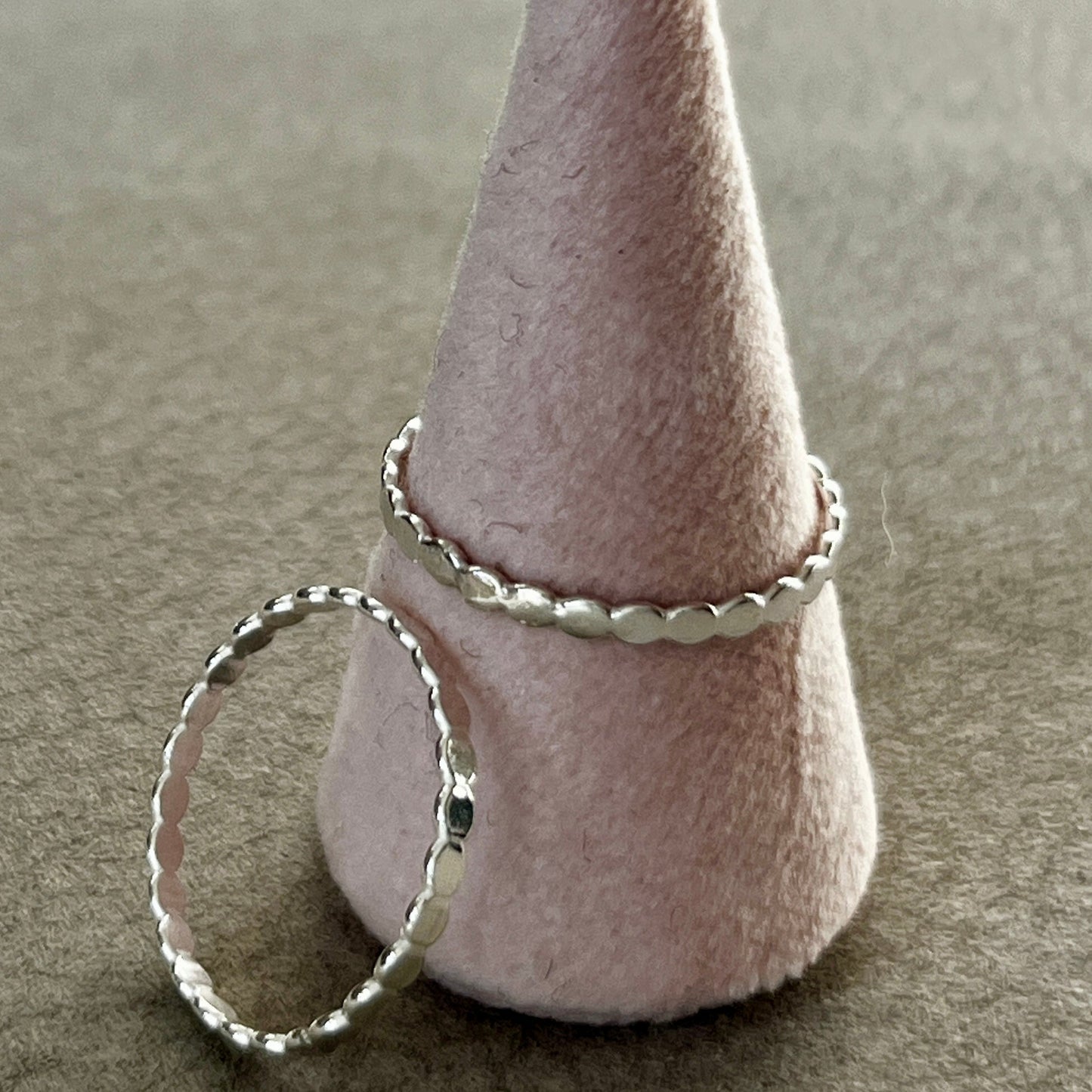 Silver ring on a cone-shaped felt stand against a neutral background
