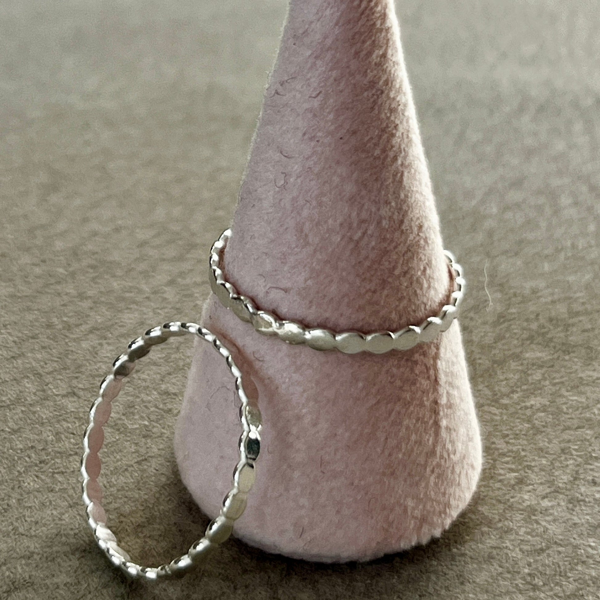 Silver ring on a cone-shaped felt stand against a neutral background