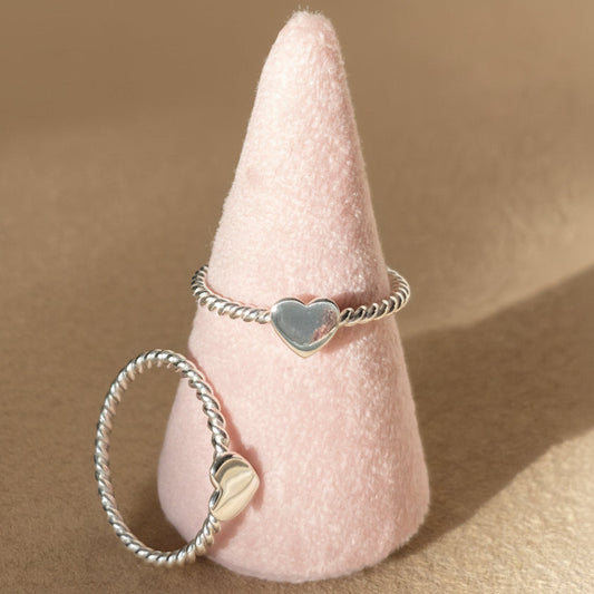 Two silver rings with heart-shaped charms on a pink cone against a gray background