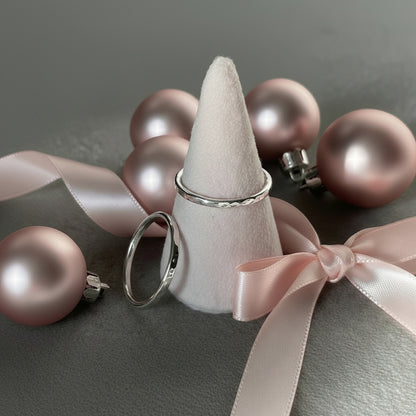 silver ring on a pink cone on a grey background with a second ring propped against the cone