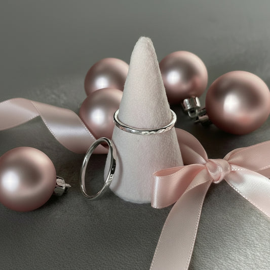 silver ring on a pink cone on a grey background with a second ring propped against the cone