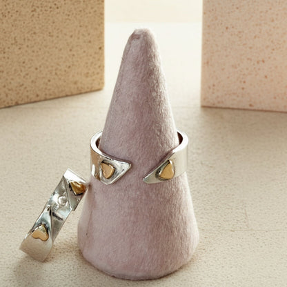 Silver ring with gold heart-shaped stones on a cone-shaped gray stand.