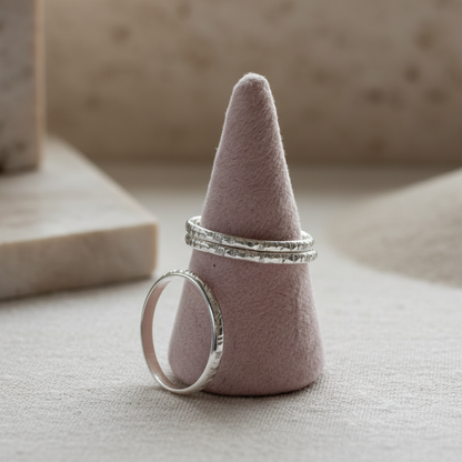 Two silver rings on a pink cone-shaped jewelry holder against a neutral background
