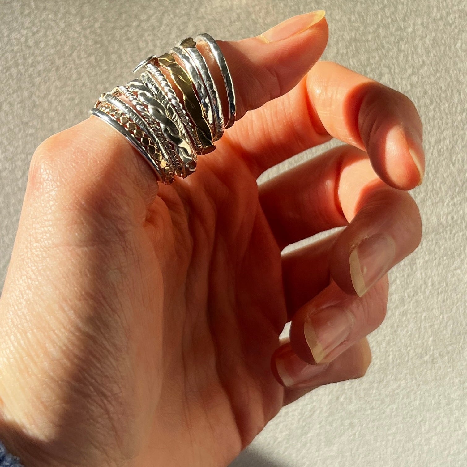 Hand wearing multiple silver rings on a neutral background