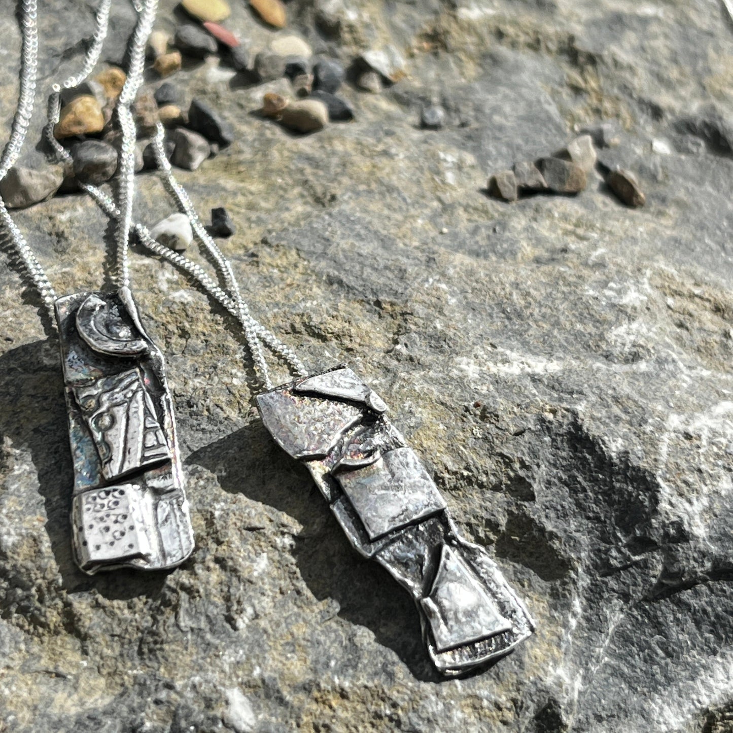 Silver necklace with decorative pendants on a rocky surface