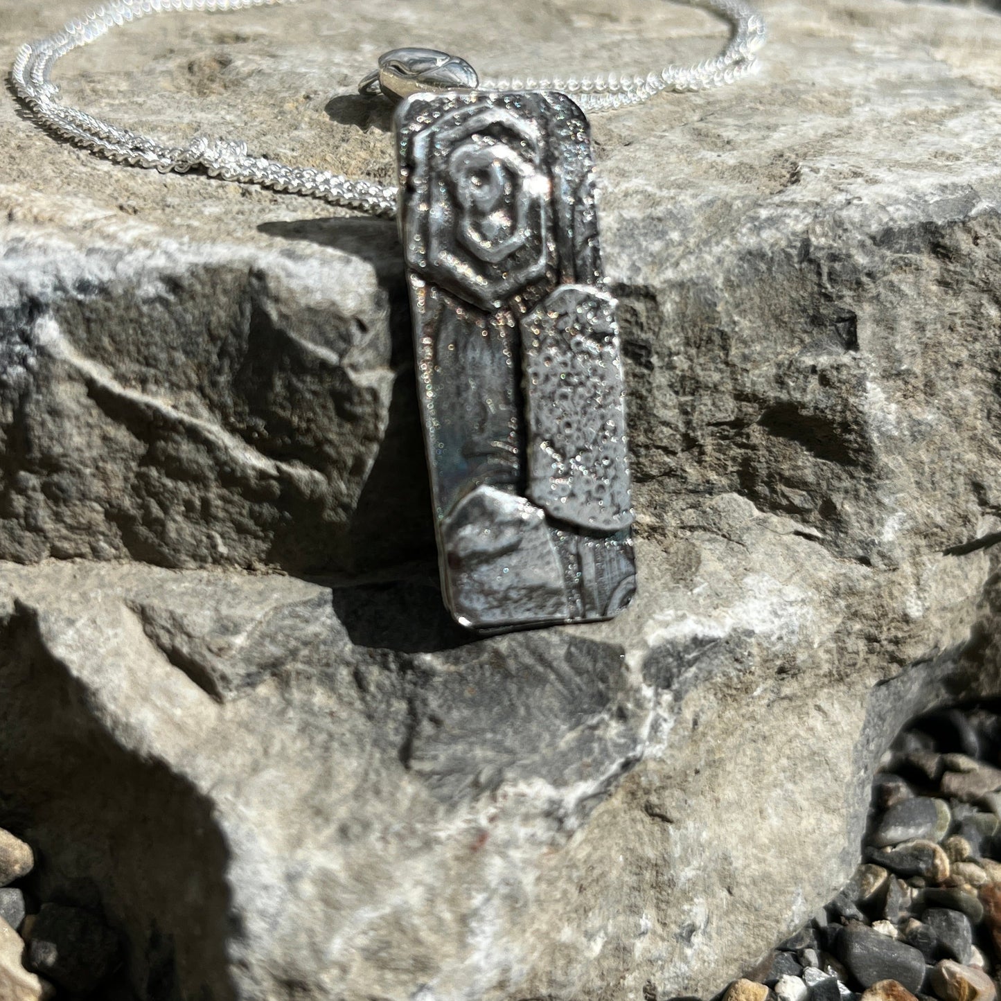 Silver pendant with a decorative band on a stone surface