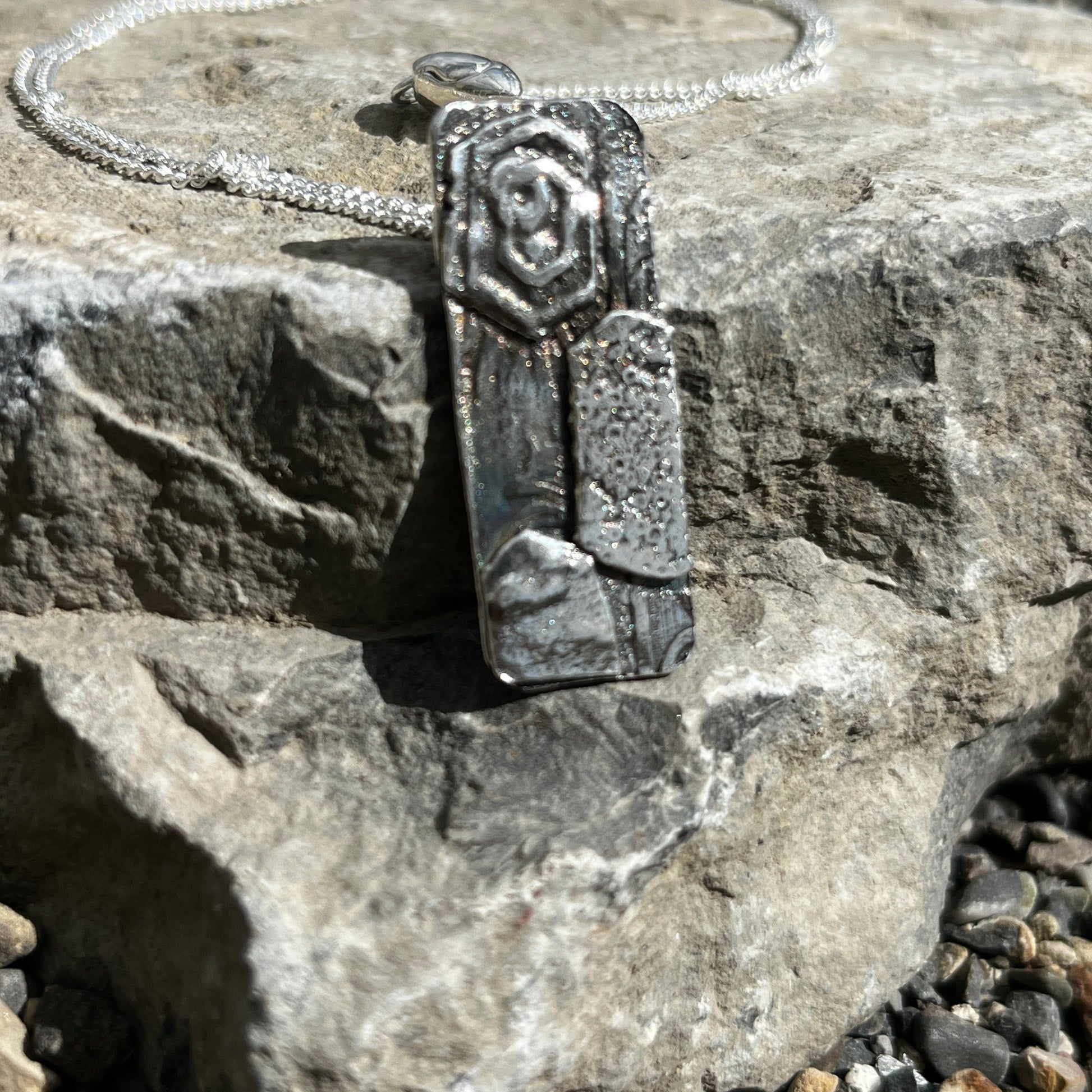 Silver pendant with a decorative band on a stone surface