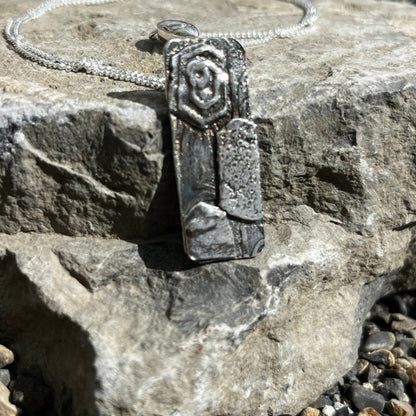 Silver pendant with a decorative band on a stone surface