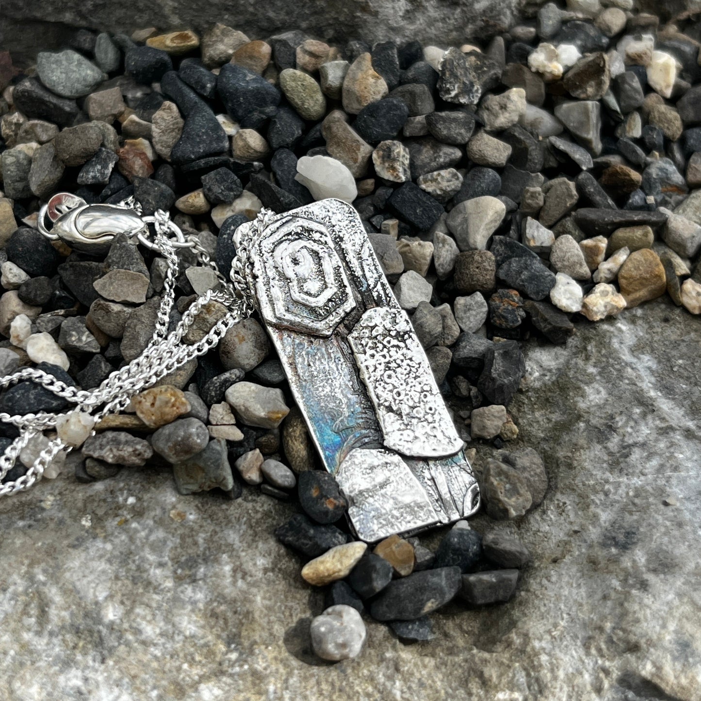 Silver necklace with a pendant on pebbles and stone surface