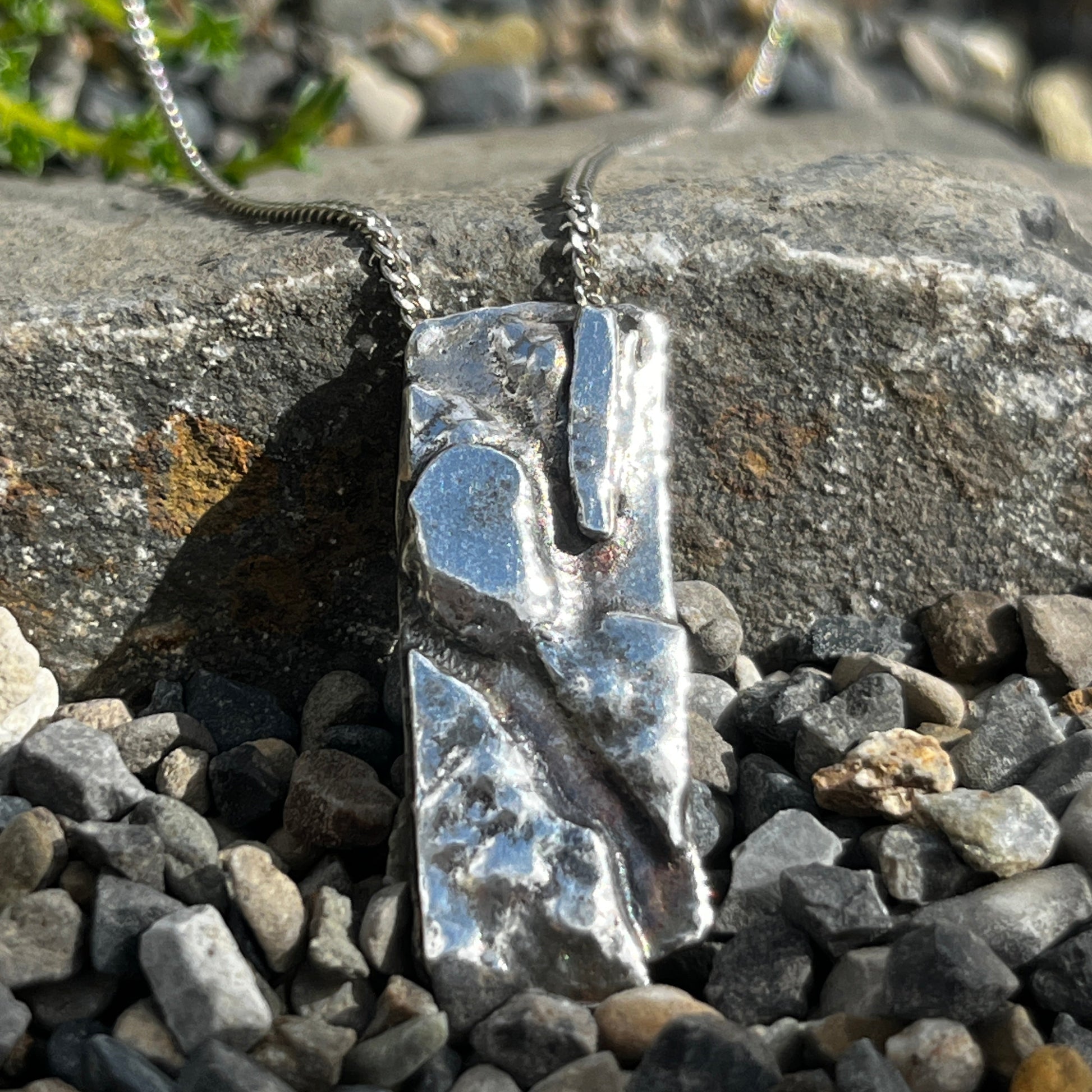 Silver necklace with a pendant on a rocky surface