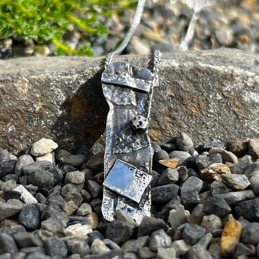 Silver bracelet on a stone surface with pebbles and grass in the background