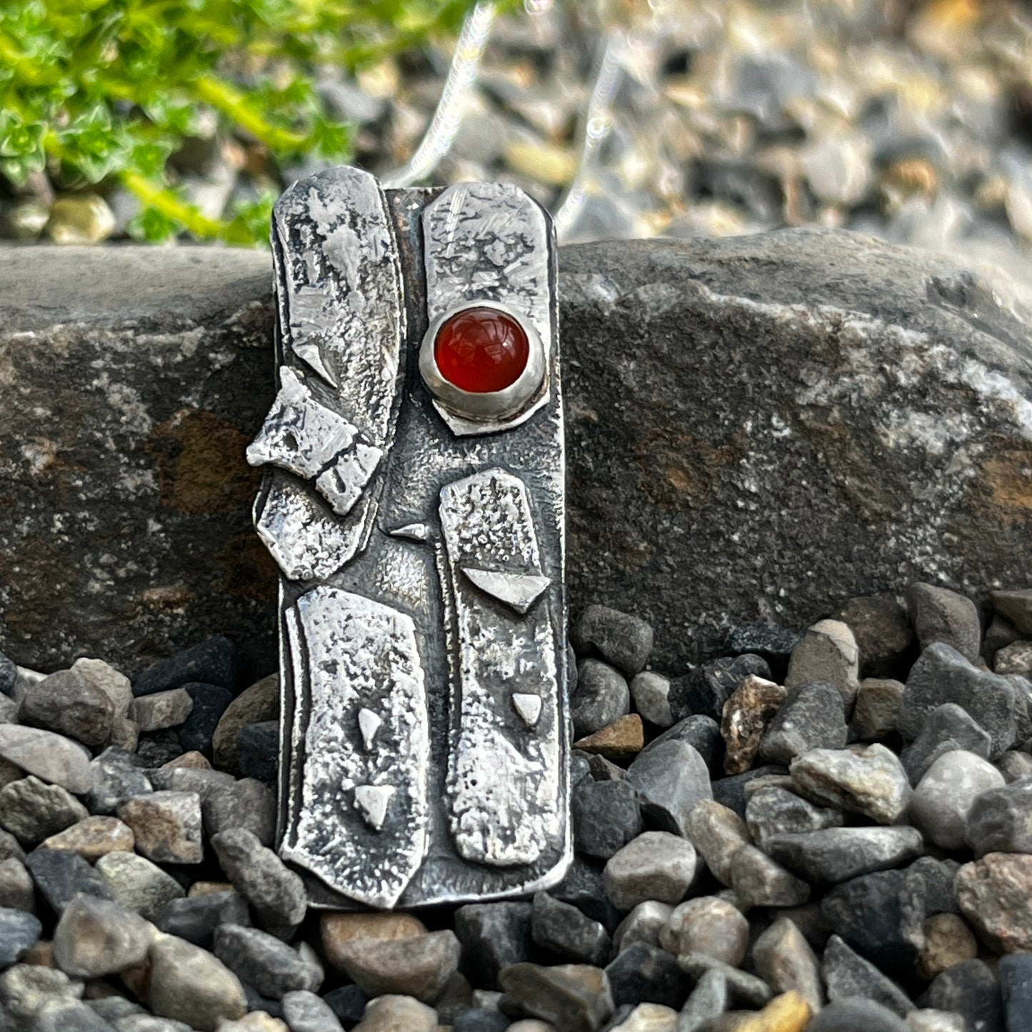 Silver pendant with an orange carnelian stone on a pebbly surface