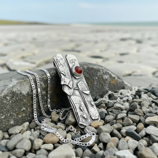 Silver pendant with an orange carnelian stone on a pebbly surface