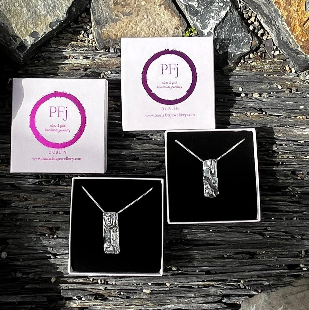 Jewelry display with necklaces and branded cards on a stone surface