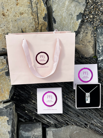 Jewelry packaging with a pink card and purple circular logo on a stone surface