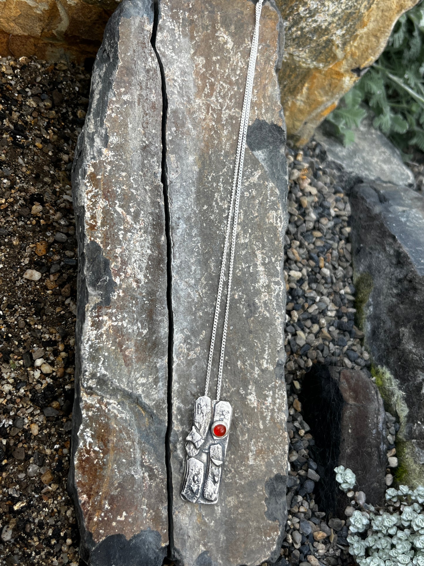 Silver necklace with red stone on a stone surface