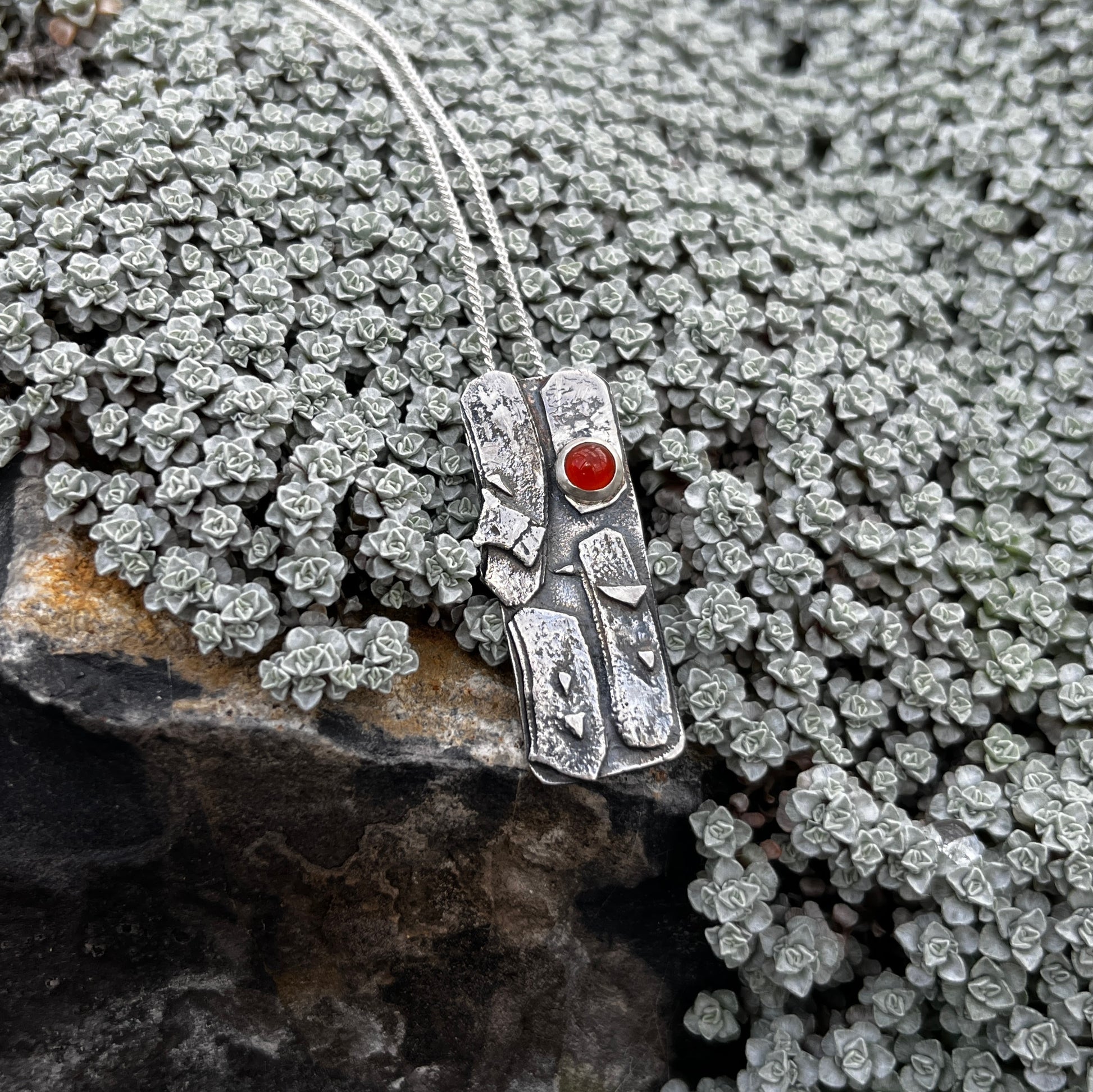 Silver pendant with a red gemstone on a rocky surface