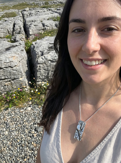 Woman wearing a necklace with a pendant in front of rocky landscape