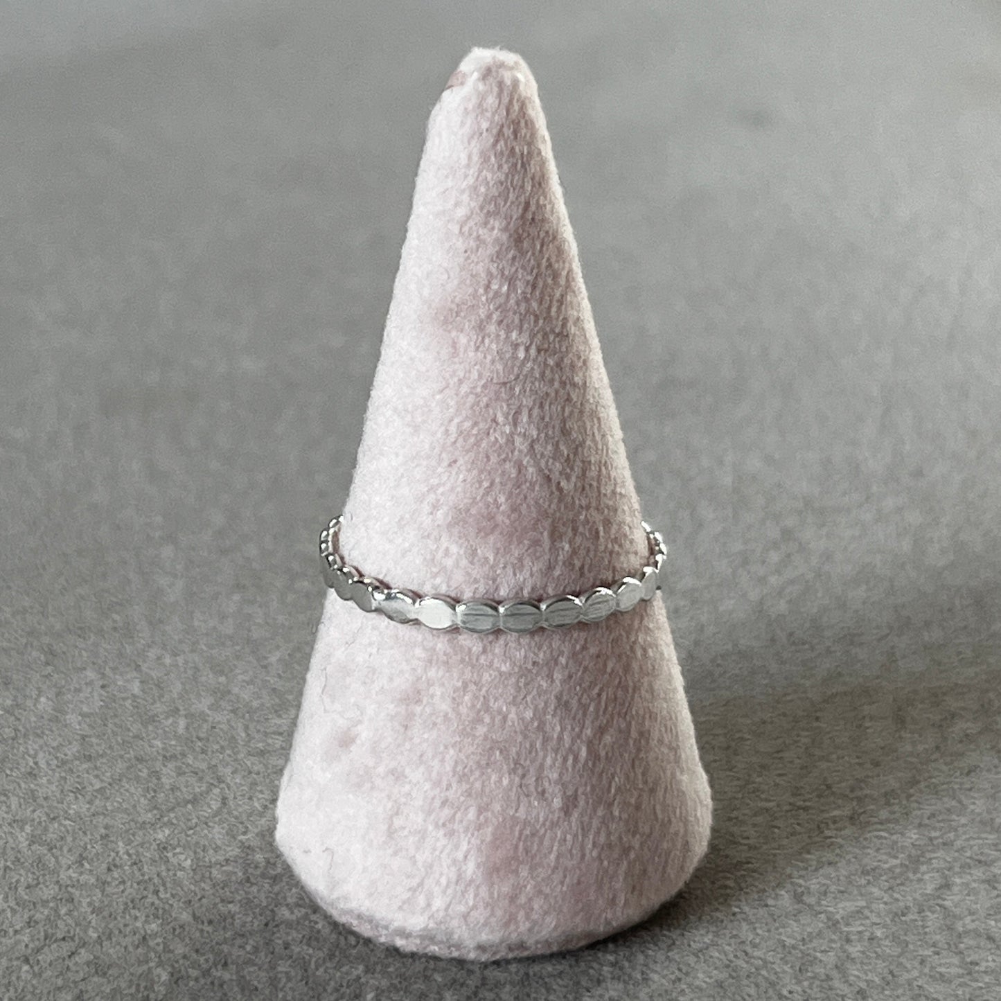 Silver ring on a cone-shaped felt stand against a gray background