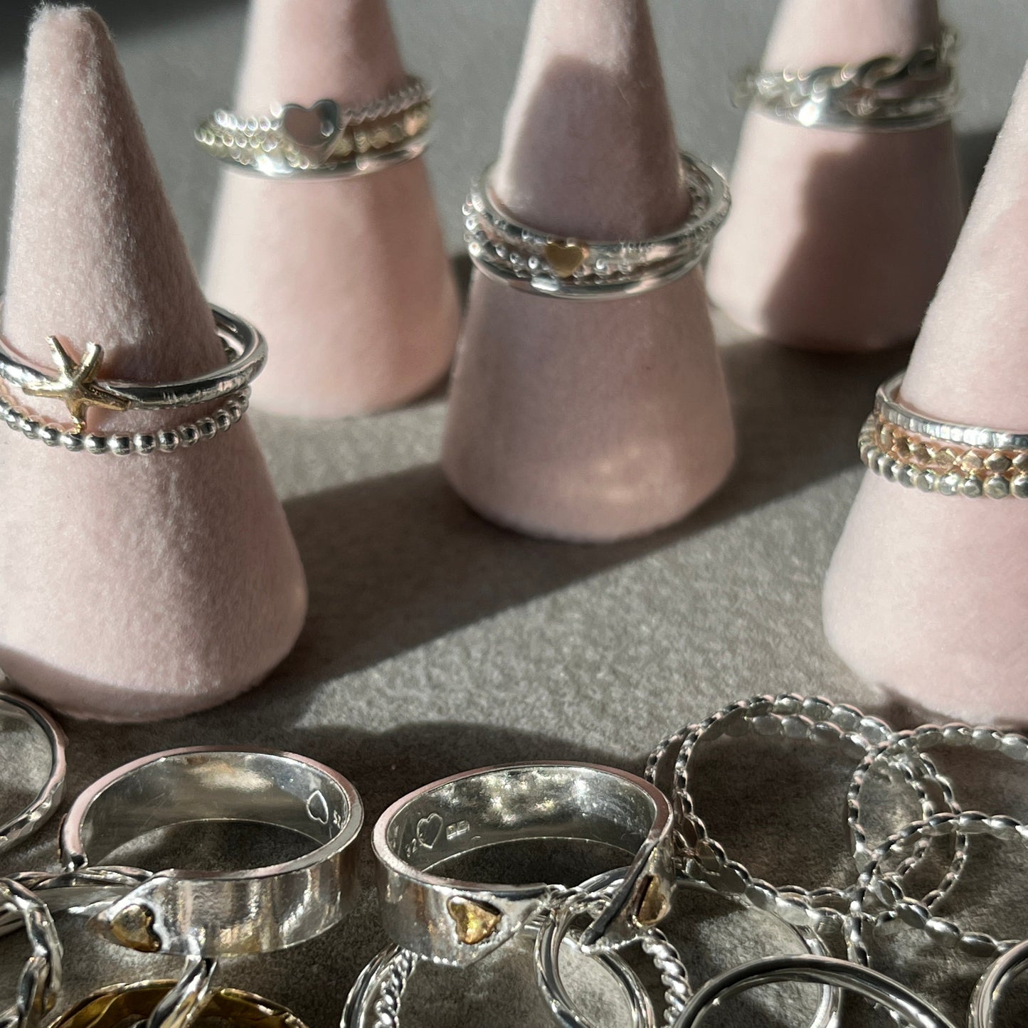 Collection of silver rings on pink cone-shaped stands with additional rings scattered below.