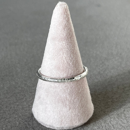 Silver ring on a white cone-shaped stand against a gray background