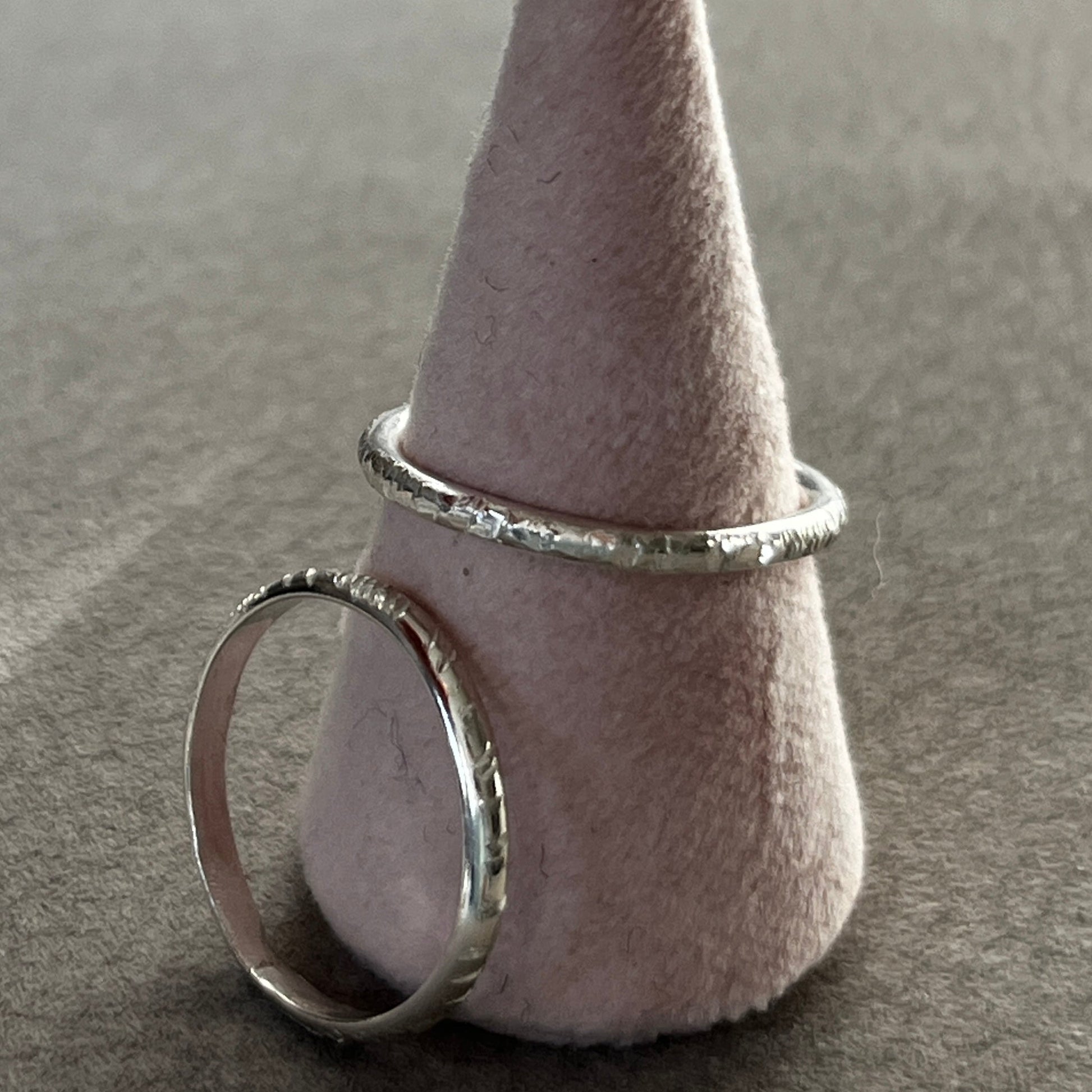 Two silver rings on a textured gray surface with a cone-shaped object.
